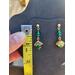 Emerald and gold post earrings hang on a jewelry display beside a tape measure. Earrings measure 1.25 inches long. 